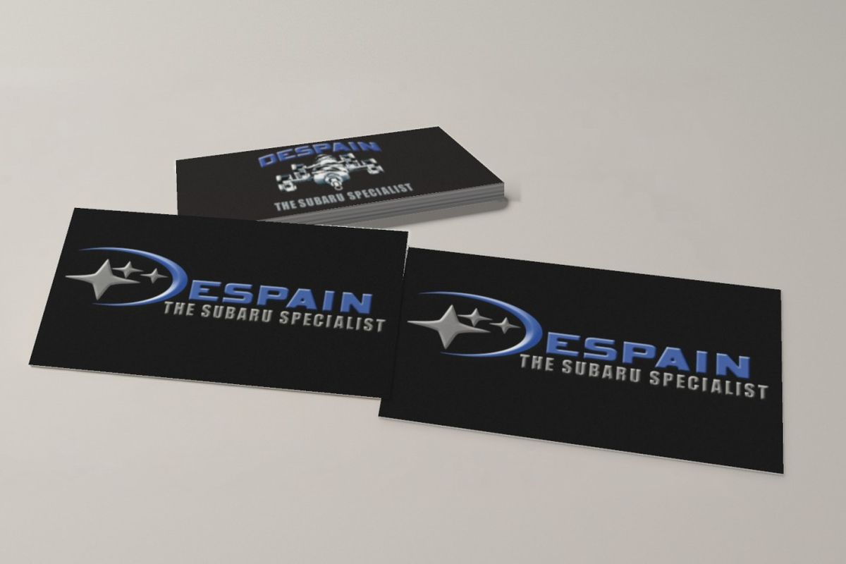 DeSpain The Subaru Specialist business cards on a light gray table: two black cards side by side, each with a silver star and blue swoosh logo, in front of a stack whose top card shows the blue DeSpain name, an engine illustration and 'The Subaru Specialist'.