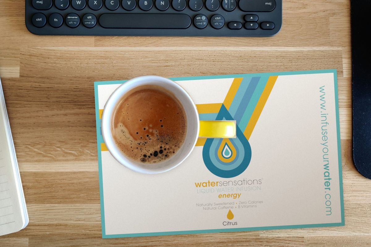 Water Sensations postcard with retro yellow and blue stripes, a water-drop logo and Citrus flavor details, on a wooden desk under a cup of coffee, beside a keyboard and notebook.
